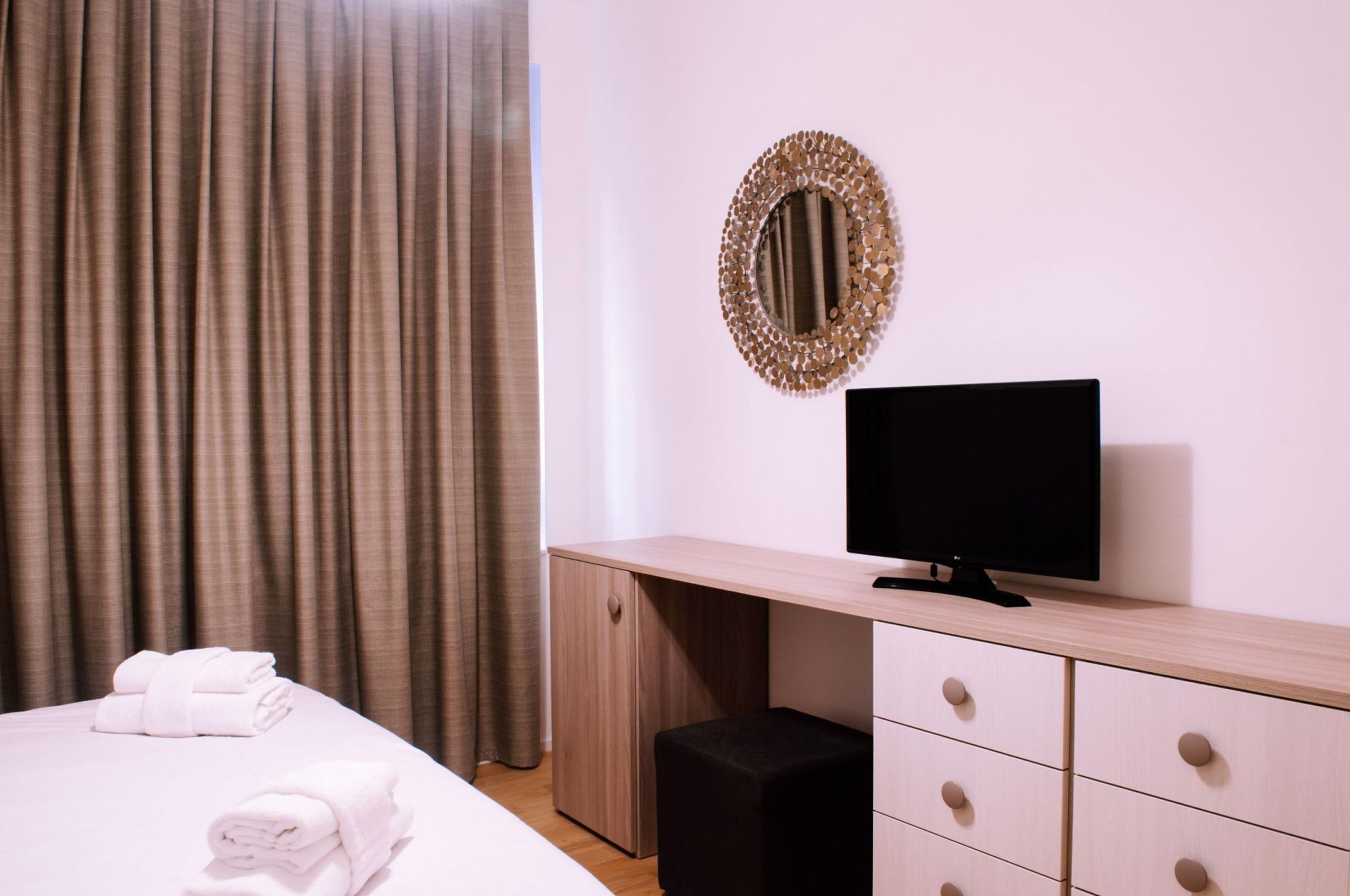 Ett hotellrum med en säng, en tv, ett skrivbord i trä och en spegel på väggen.