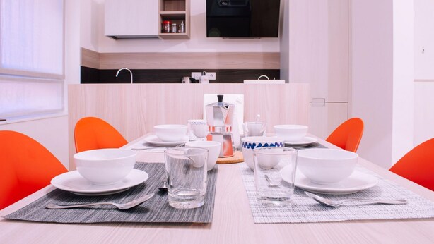 A dining area with a table set for four, surrounded by orange chairs, with a kitchen area visible in the background. - Design Apartment Alle due Torri by Wonderful Italy (Bologna)