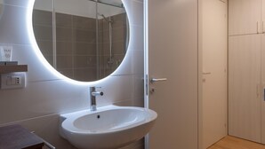 A modern bathroom with a round mirror, a white sink, and a shower enclosure. - Design Apartment Alle due Torri by Wonderful Italy (Bologna)