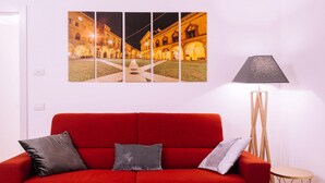 A red sofa with two pillows, a floor lamp, and a triptych painting of a building at night. - Design Apartment Alle due Torri by Wonderful Italy (Bologna)