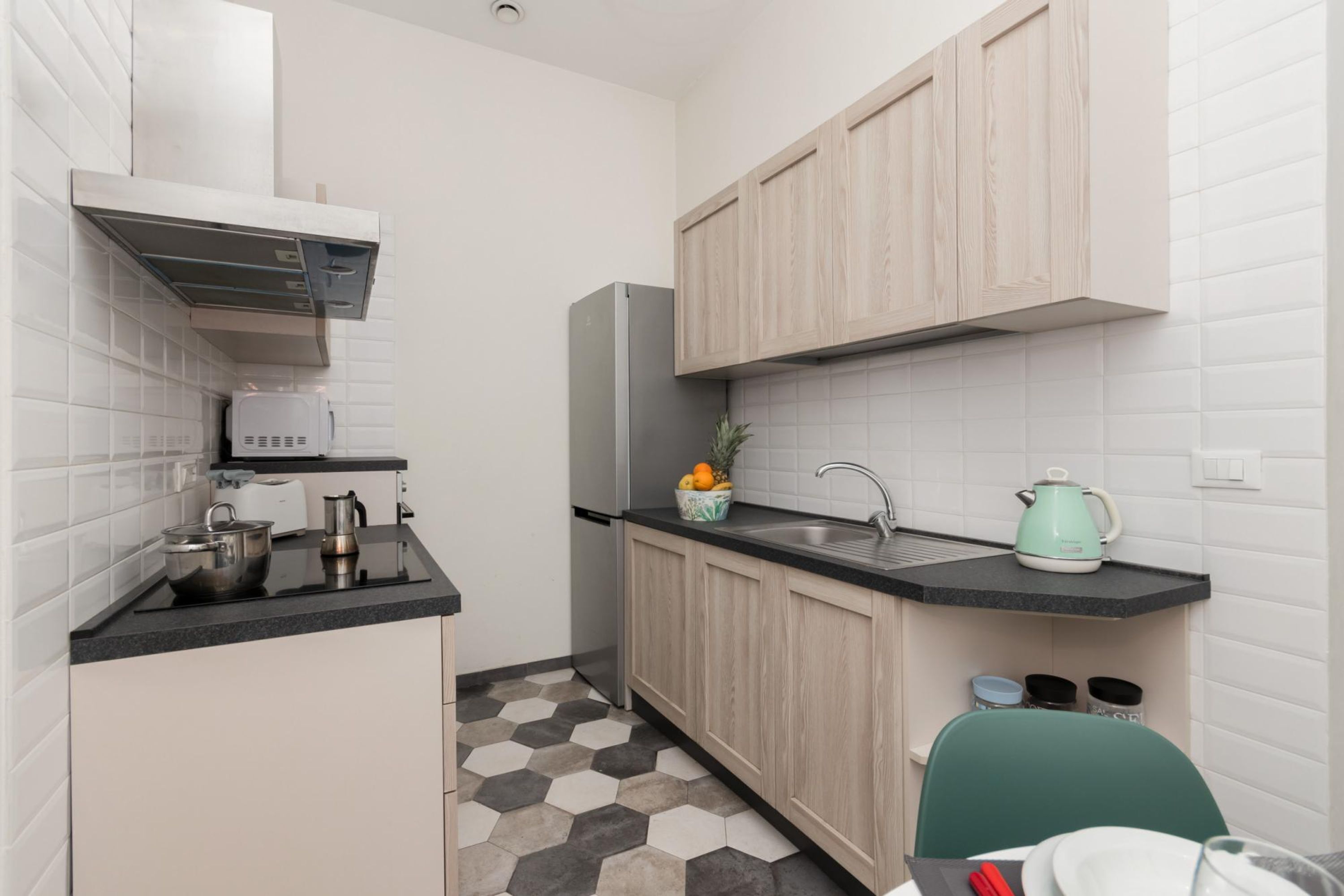 A compact kitchen with white cabinets, a black countertop, and a hexagonal patterned floor.