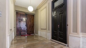 Um corredor com piso de pedra polida, uma porta de madeira e uma porta preta com puxador.
