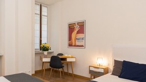 Quarto com duas camas, uma escrivaninha, uma cadeira, um criado-mudo e um quadro na parede.