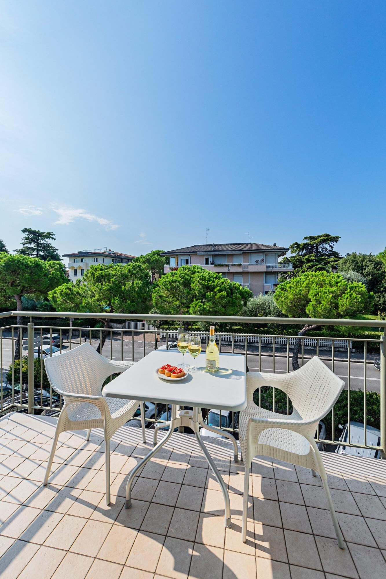A balcony with a table, two chairs, a bottle of wine, and a plate of food.