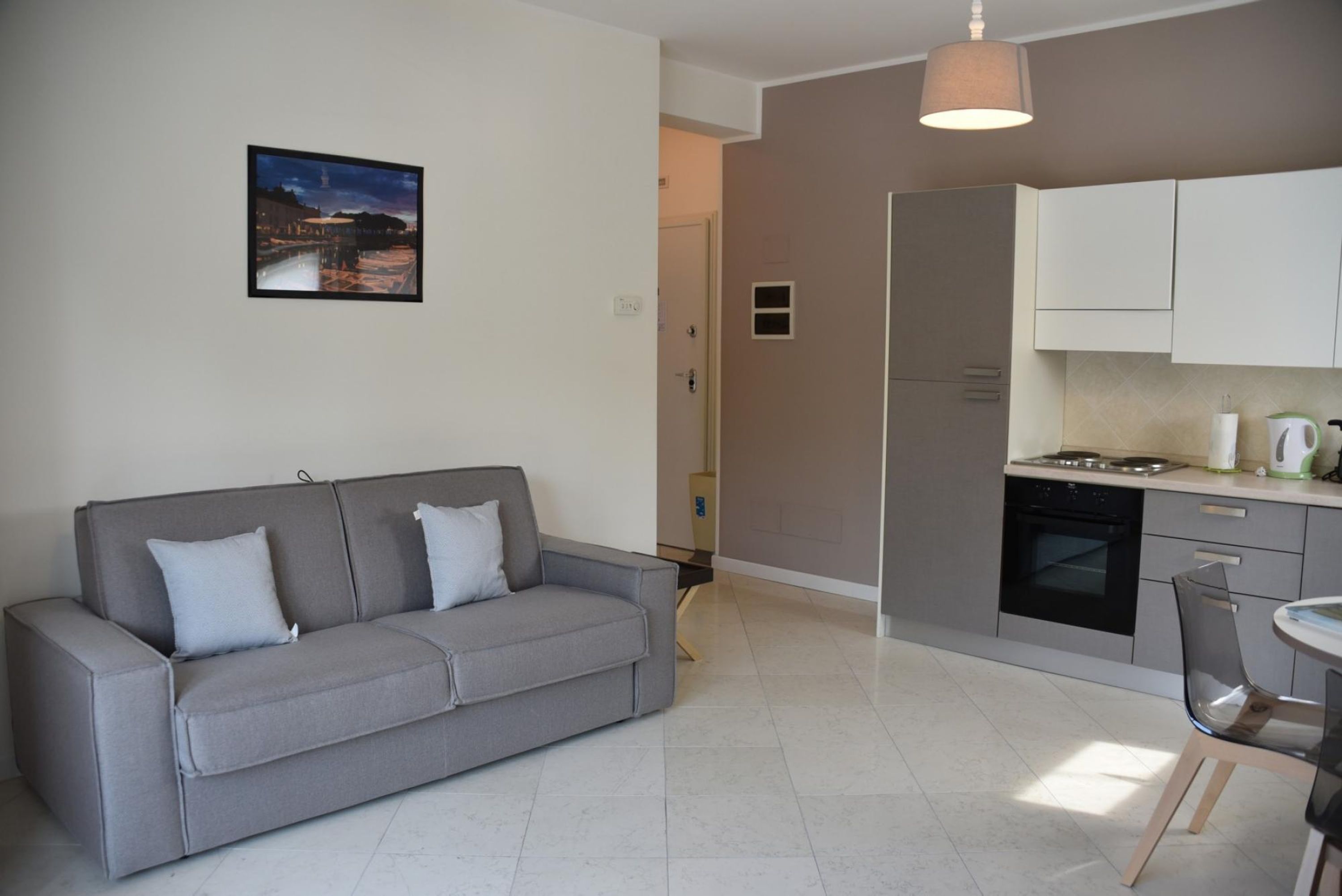 A modern living room with a grey sofa, a dining area with a table and chairs, and a kitchen with white cabinets and a stove.