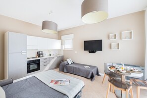 A modern hotel room with two beds, a kitchenette, a dining area, and a TV.