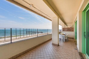 A balcony with a view of the sea, a table with chairs, and a green door.