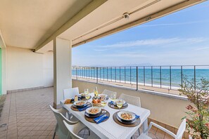 Ein Balkon mit Tisch, gedeckt für eine Mahlzeit, mit Blick auf einen Strand und das Meer.