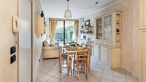 A dining area with a table set for four, surrounded by wooden chairs. There is a sofa in the background, and a cabinet with glass doors to the right.