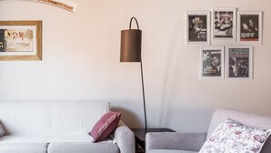 Una sala de estar con un sofá gris, una lámpara de pie y carteles de películas enmarcados en la pared.