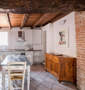 A kitchen with white cabinets, a wooden dining table, and a brick wall. - Appartamento San Martino by Wonderful Italy (Bologna)