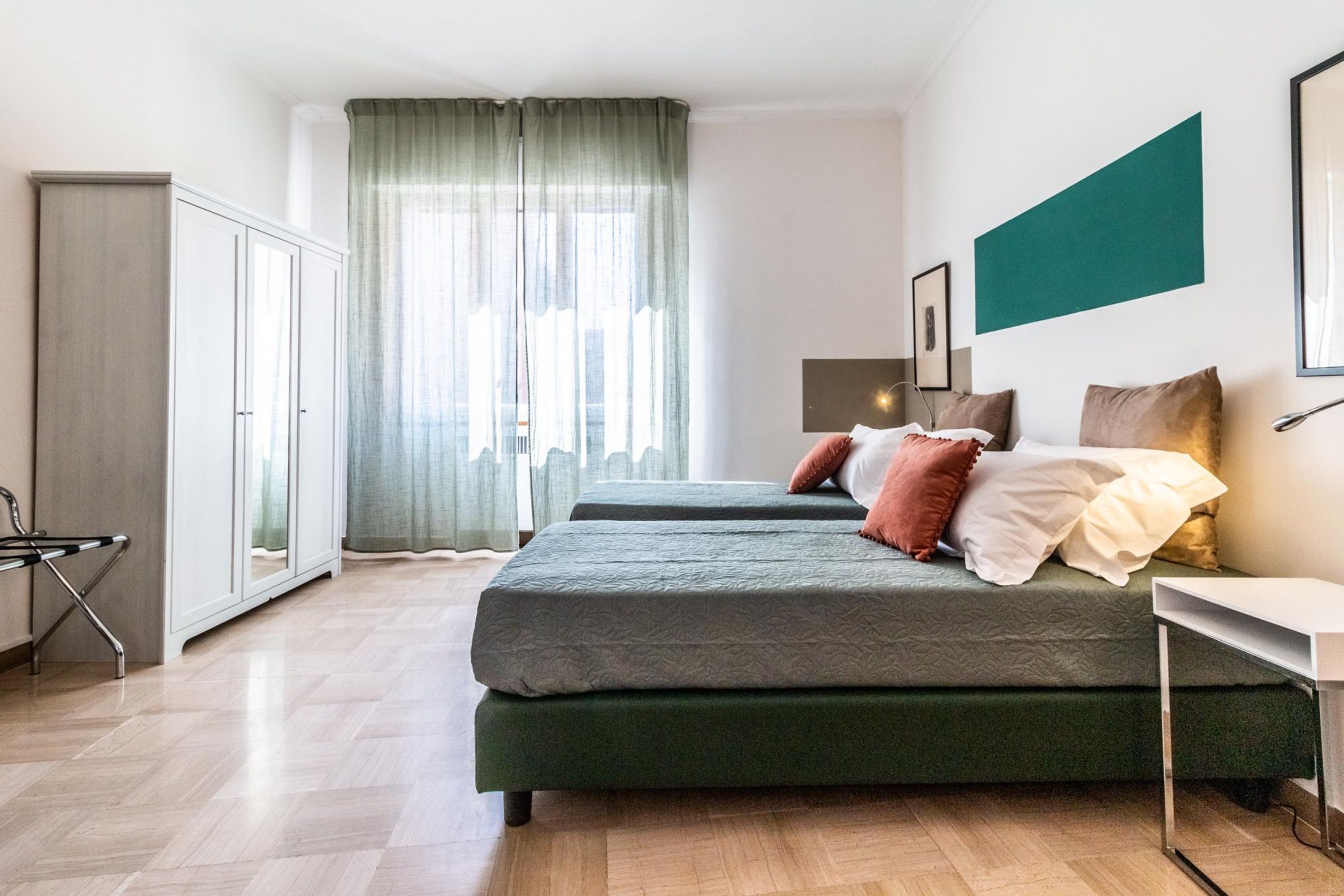 A modern bedroom with two beds, a desk, and a wardrobe.