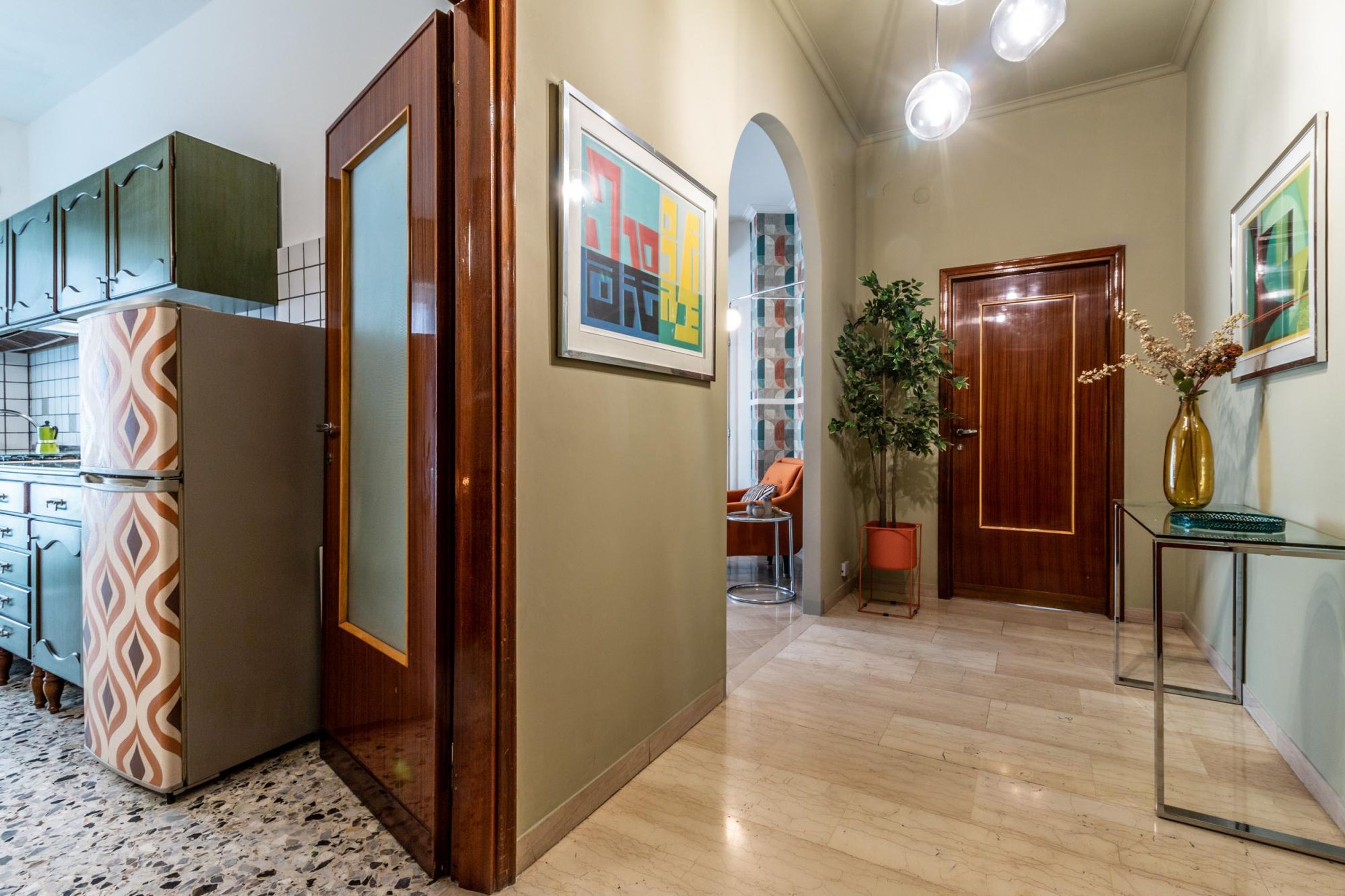 A modern kitchen with patterned appliances, a wooden door, and a hallway leading to a seating area.