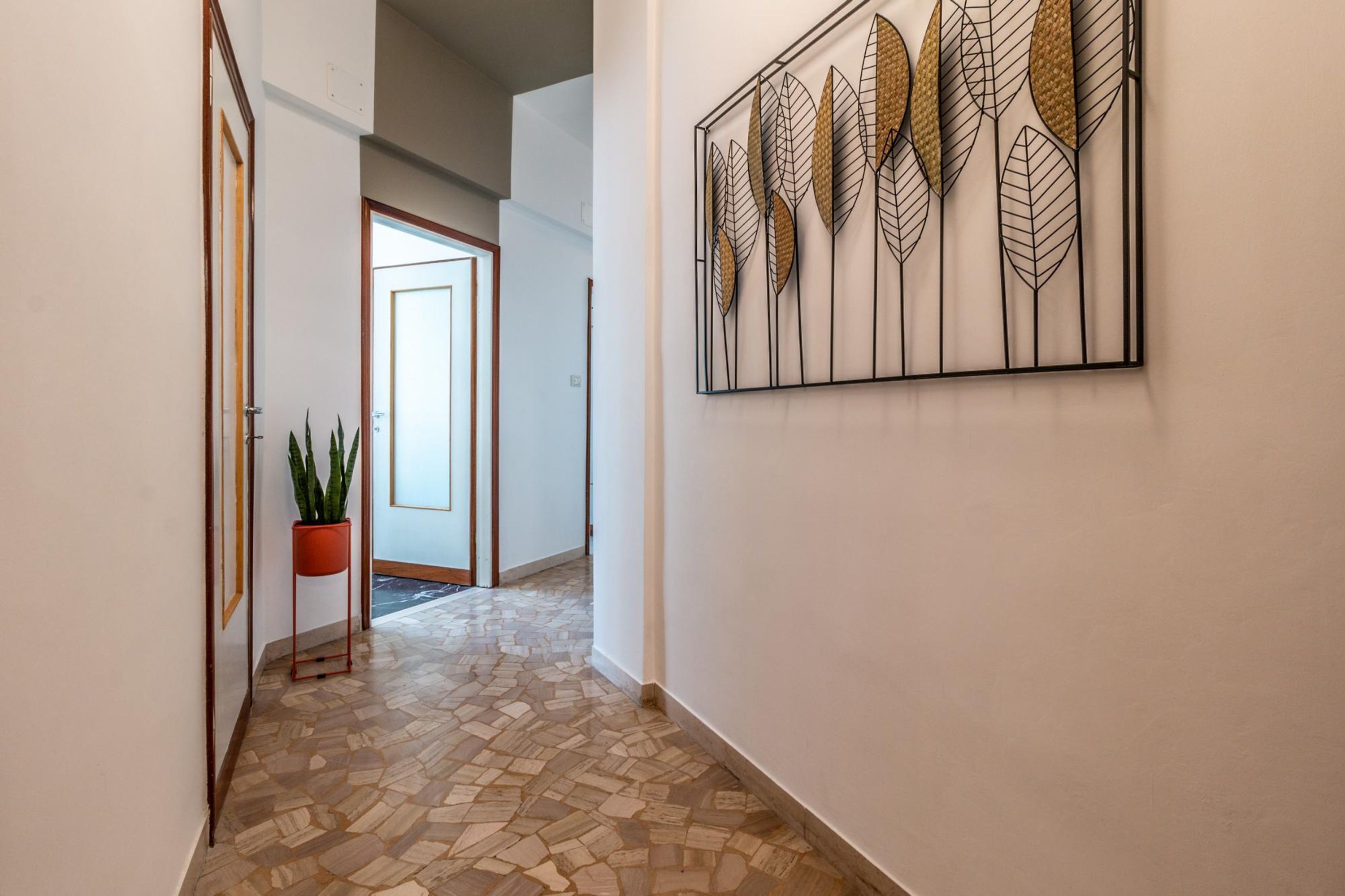 A hallway with a patterned floor, a potted plant, and a wall-mounted artwork.