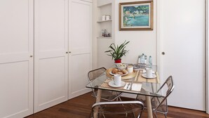 A dining area with a glass table, chairs, a potted plant, and a painting on the wall. - Elegant Studio in the City Center by Wonderful Italy (Genoa)