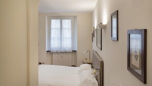 A bedroom with a bed, a window with curtains, a bedside table with a lamp, and framed pictures on the wall. - Elegant Studio in the City Center by Wonderful Italy (Genoa)
