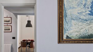 Um corredor com área de jantar, apresentando uma mesa com cadeiras, uma luminária pendente preta e quadros nas paredes.