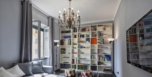 Un salon moderne avec un canapé gris, une grande bibliothèque et un lustre.