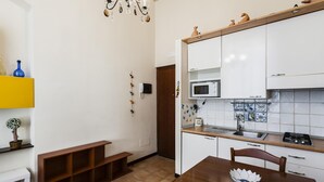 A compact kitchen with white cabinets, a microwave, and a tiled backsplash. - Grimaldi 8 Apartment by Wonderful Italy (Catania)