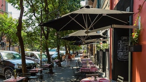Een terras met tafels en stoelen, parasols en een straatbeeld.