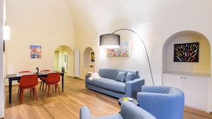 Een moderne woonkamer met een bank, twee fauteuils, een eettafel met stoelen en een keukenhoek.