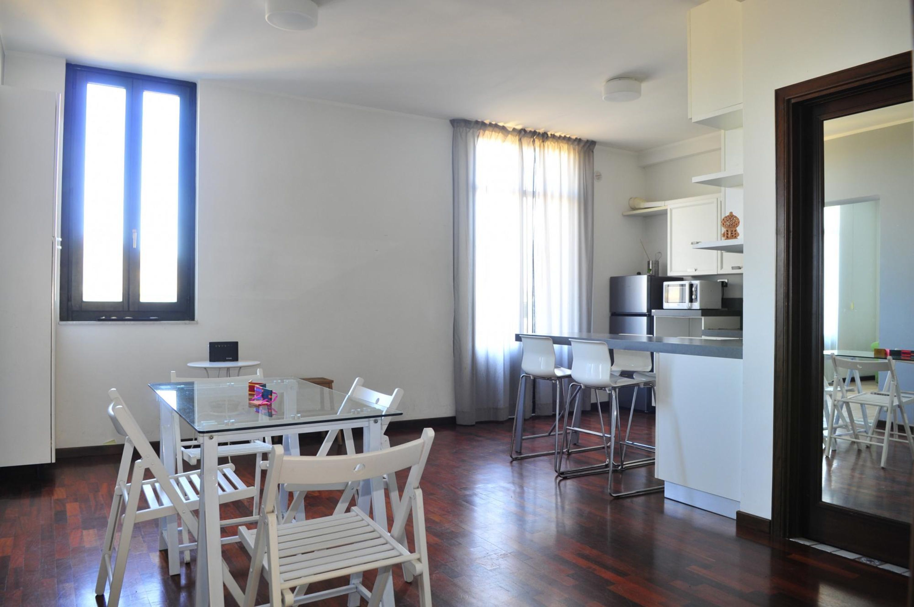 Una cocina moderna con armarios blancos, un microondas y un pequeño comedor con una mesa de vidrio y sillas blancas.