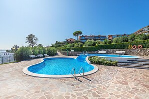 Une piscine avec une terrasse en pierre, une vue sur la mer et un bâtiment en arrière-plan.