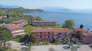 A residential area with multiple apartment buildings, a well-maintained lawn, and a view of a large body of water. - San Sivino 42 con Piscina by Wonderful Italy (Manerba del Garda)
