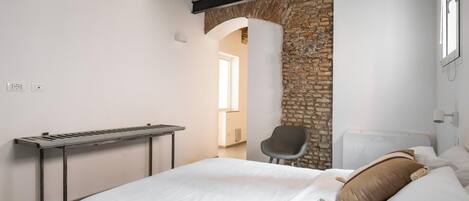 Una camera da letto con un letto, una sedia, una scrivania e un muro in pietra.