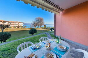 Una mesa preparada para una comida, con platos y bebidas, con vistas a un cuerpo de agua y un edificio con balcones.