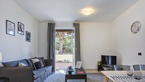 A modern living room with a sofa, coffee table, TV, and a dining area with chairs and a table. - Shelley Apartments - Tree by Wonderful Italy (Genoa)