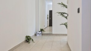 A clean, modern hallway with a sign reading "SHELLEY" on the floor, potted plants, and a door at the end. - Shelley Apartments - Tree by Wonderful Italy (Genoa)