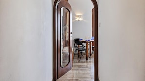 Un couloir mène à une salle à manger où se trouvent une table et des chaises, une porte en bois et un luminaire fixé au mur.