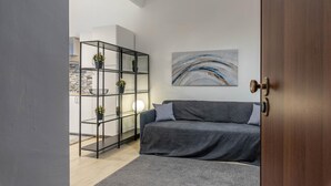 Un salon moderne avec un canapé gris, une étagère noire ornée de plantes et un tableau accroché au mur.