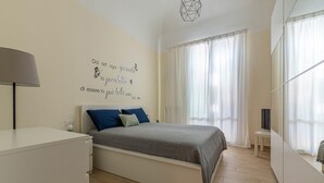Une chambre à coucher comprenant un lit, une table de chevet, une lampe, un téléviseur et un mur orné d’un texte motivant.