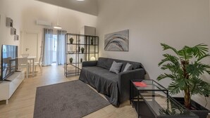 Un salon moderne avec un canapé gris, une table basse en verre, un téléviseur à écran plat et une plante en pot.