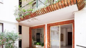 Un patio con suelo estampado, un balcón con plantas y la entrada de un edificio.