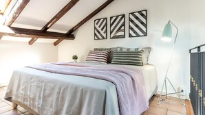A bedroom with a bed, pillows, a bedside lamp, and a wall with three geometric-patterned pictures. - Barbieri23 Design by Wonderful Italy (Bologna)