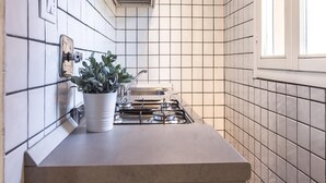A kitchen with white tiled walls, a gas stove, and a potted plant on the counter. - Barbieri23 Design by Wonderful Italy (Bologna)