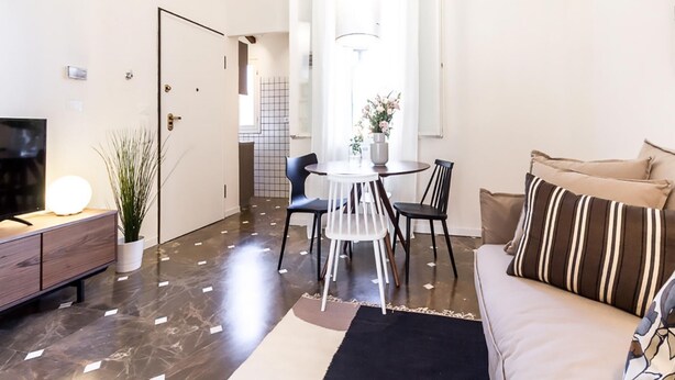 A modern living room with a sofa, a TV, a dining table with chairs, and a potted plant. - Barbieri23 Design by Wonderful Italy (Bologna)