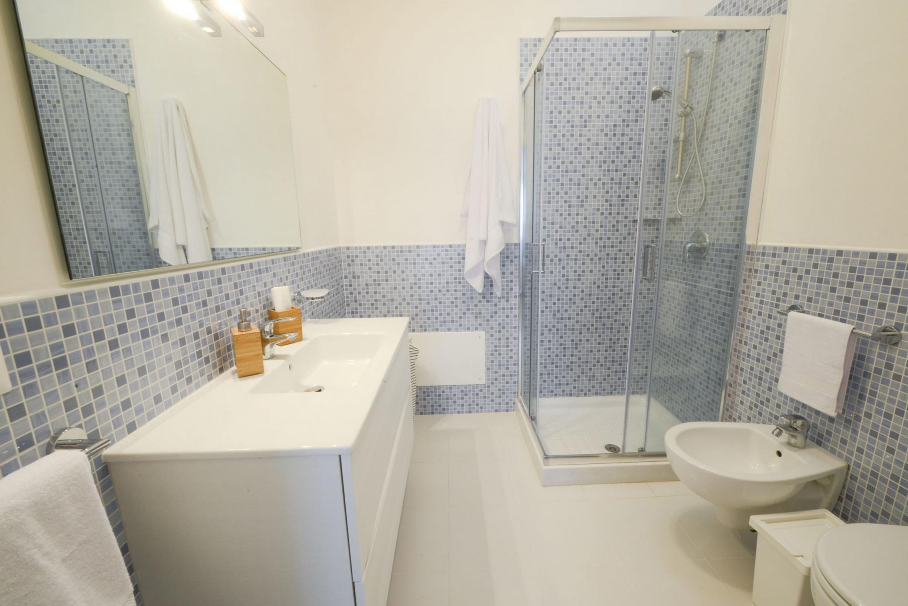 A bathroom with a white sink, a bidet, a glass-enclosed shower, and a toilet.