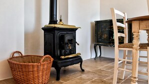 A room with a black wood-burning stove, a wicker basket, and a wooden chair.