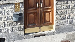 Eine Holztür mit doppelten Flügeln und einem Glasfenster darüber, eingebaut in ein Steinhaus, mit der Hausnummer '12' über der Tür.
