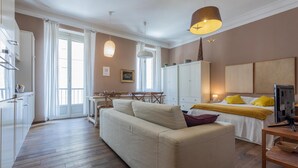 Ein modernes Wohnzimmer mit einer Couch, einem Esstisch und einem Bett mit gelben Kissen.