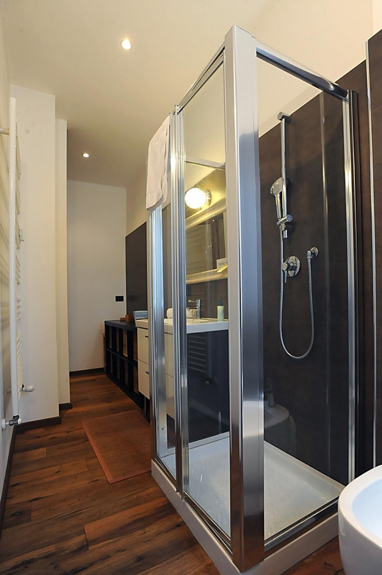 A modern bathroom with a glass-enclosed shower, a white sink, and a wooden floor.