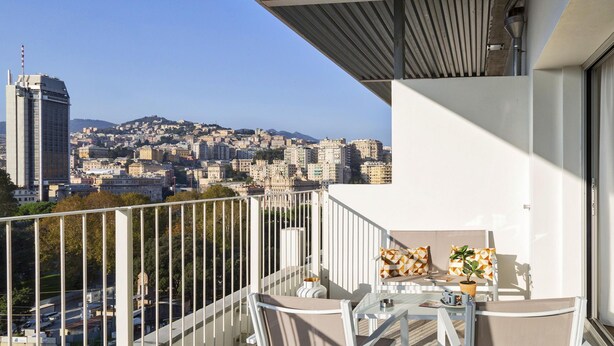 Ein Balkon mit Blick auf die Stadt, weiße Möbel und ein Tisch mit einer Pflanze.
