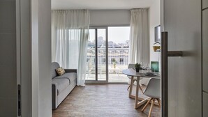 Ein modernes Wohnzimmer mit grauem Sofa, einem Esstisch mit Stühlen und Blick auf die Stadt durch große Fenster.
