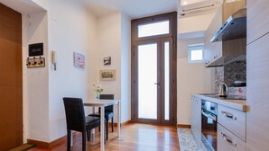 A compact kitchen with wooden cabinets, a dining table with chairs, and a large window. - Ai Piedi Della Collina by Wonderful Italy (Turin)