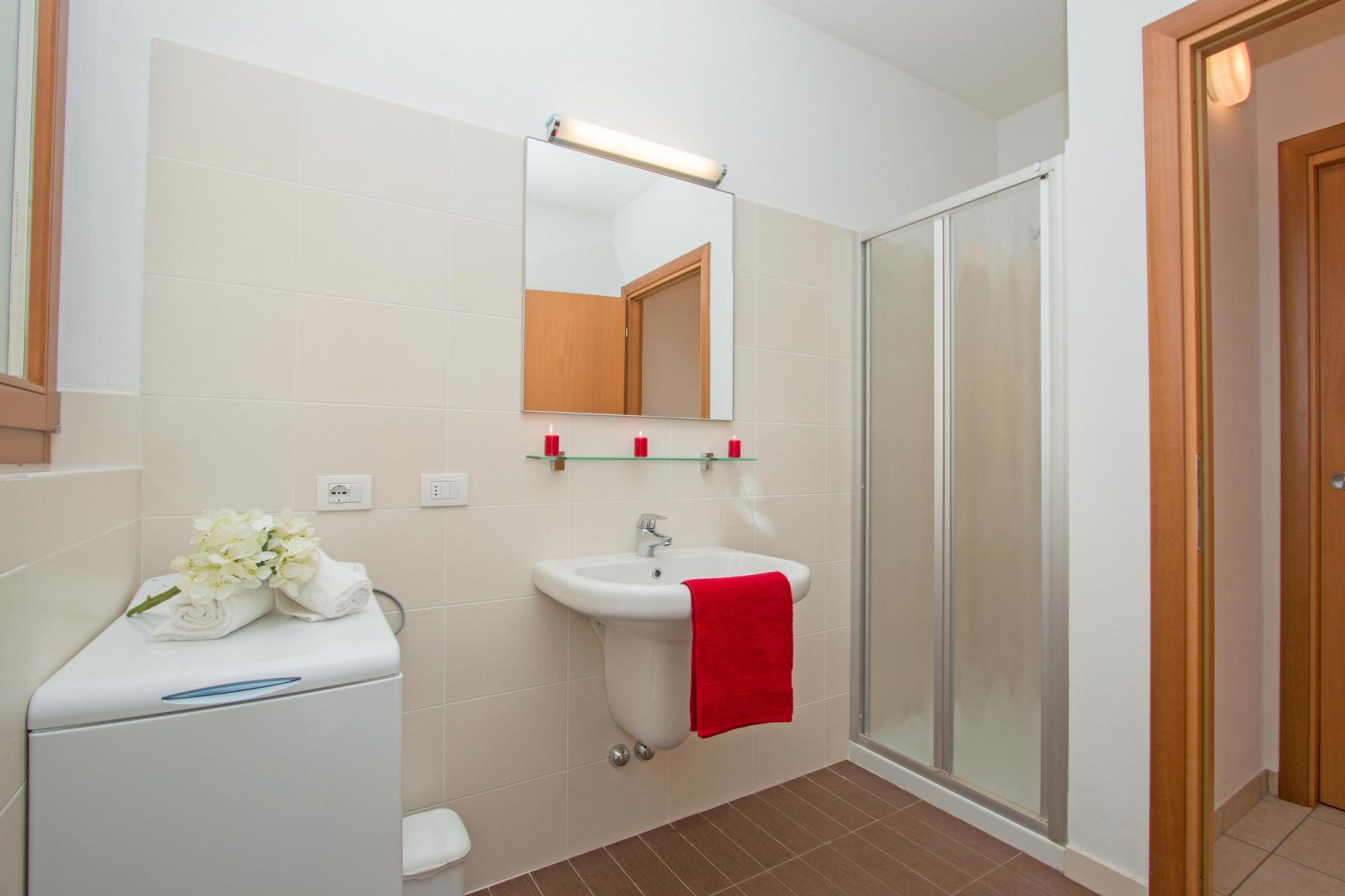 A bathroom with a white toilet, a sink with a red towel, a mirror, and a glass shower enclosure.