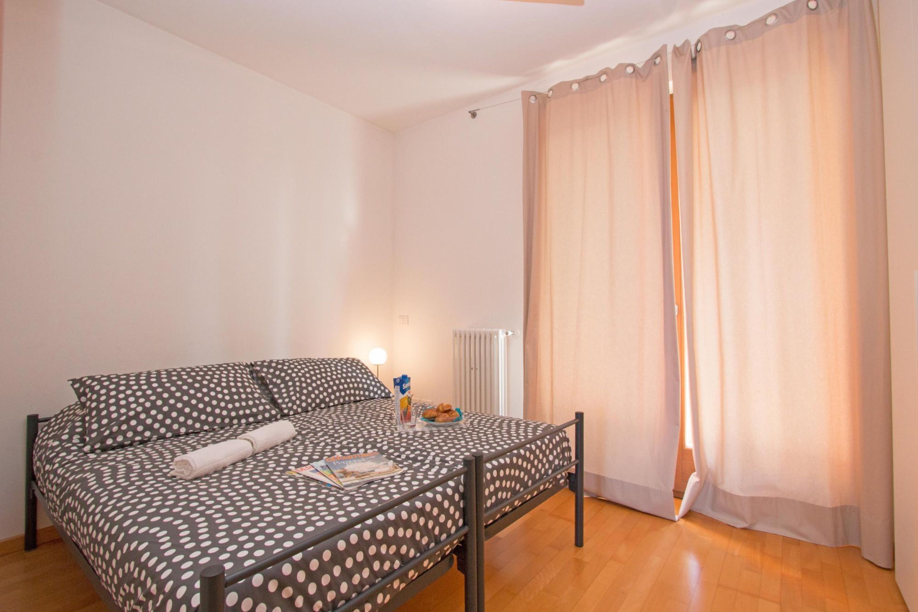 A single bed with a polka dot bedspread, a bedside table with a lamp, and a window with curtains.